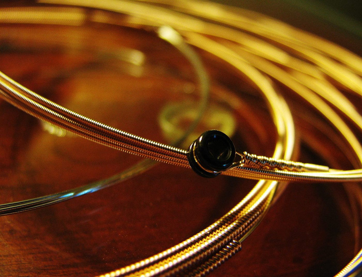 A coil of Zager phosphor bronze acoustic strings with a black ball end, resting on the wooden body of a guitar